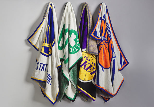 Four sports-themed blankets hanging on a gray wall, featuring Los Angeles Lakers, Boston Celtics, Golden State Warriors, and New York Knicks designs.